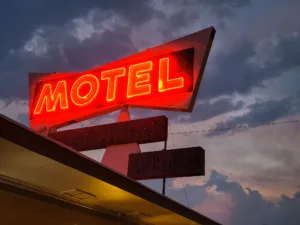 Low angle shot of red neon motel sign against dark cloudy sky background